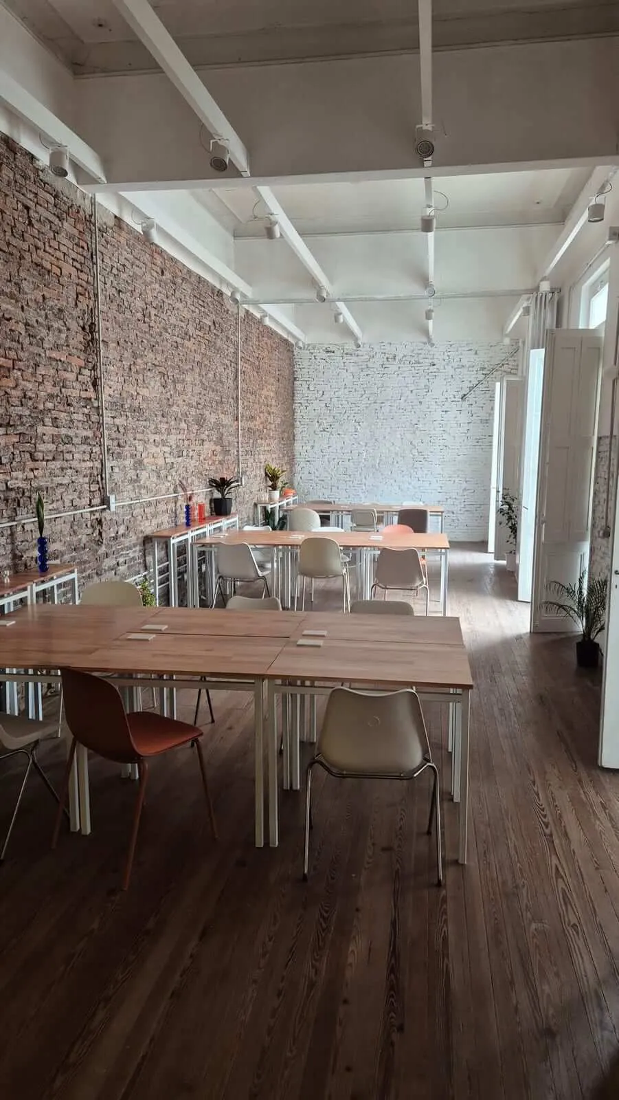 El salón de trabajo de La Casa, con mesas de madera, muro de ladrillo visto y techo alto
